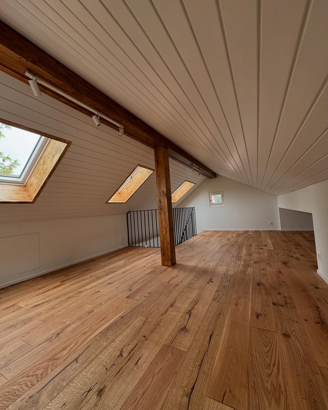 Combles aménagés avec parquet en chêne, plafond en lambris blanc et fenêtres de toit